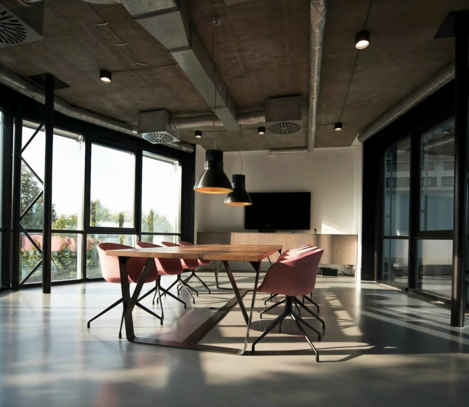 Open-plan office meeting area with large windows and pendant lights